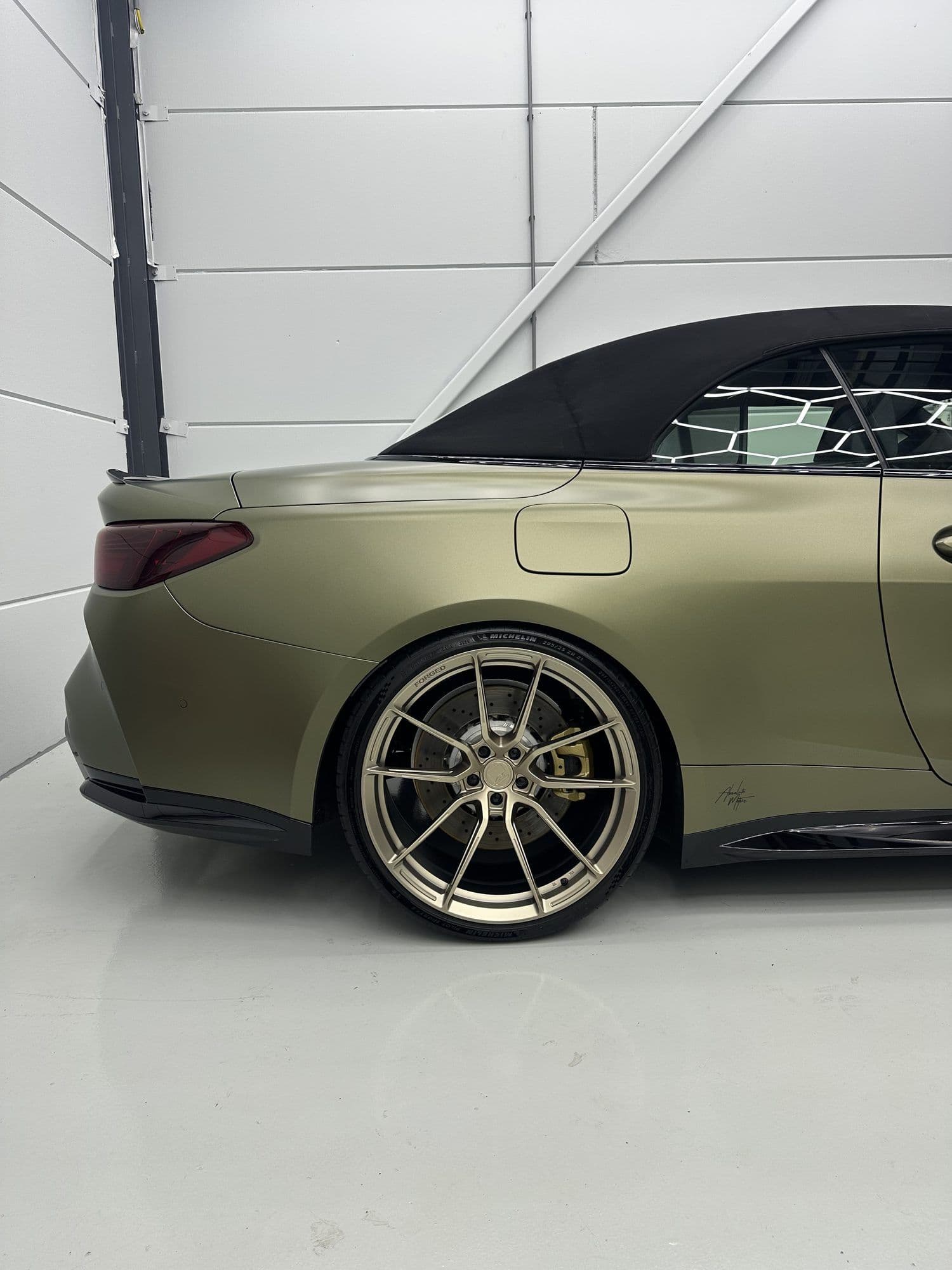 Achterkant van de matte olijfgroene BMW M4 Competition Cabrio op bronzen velgen