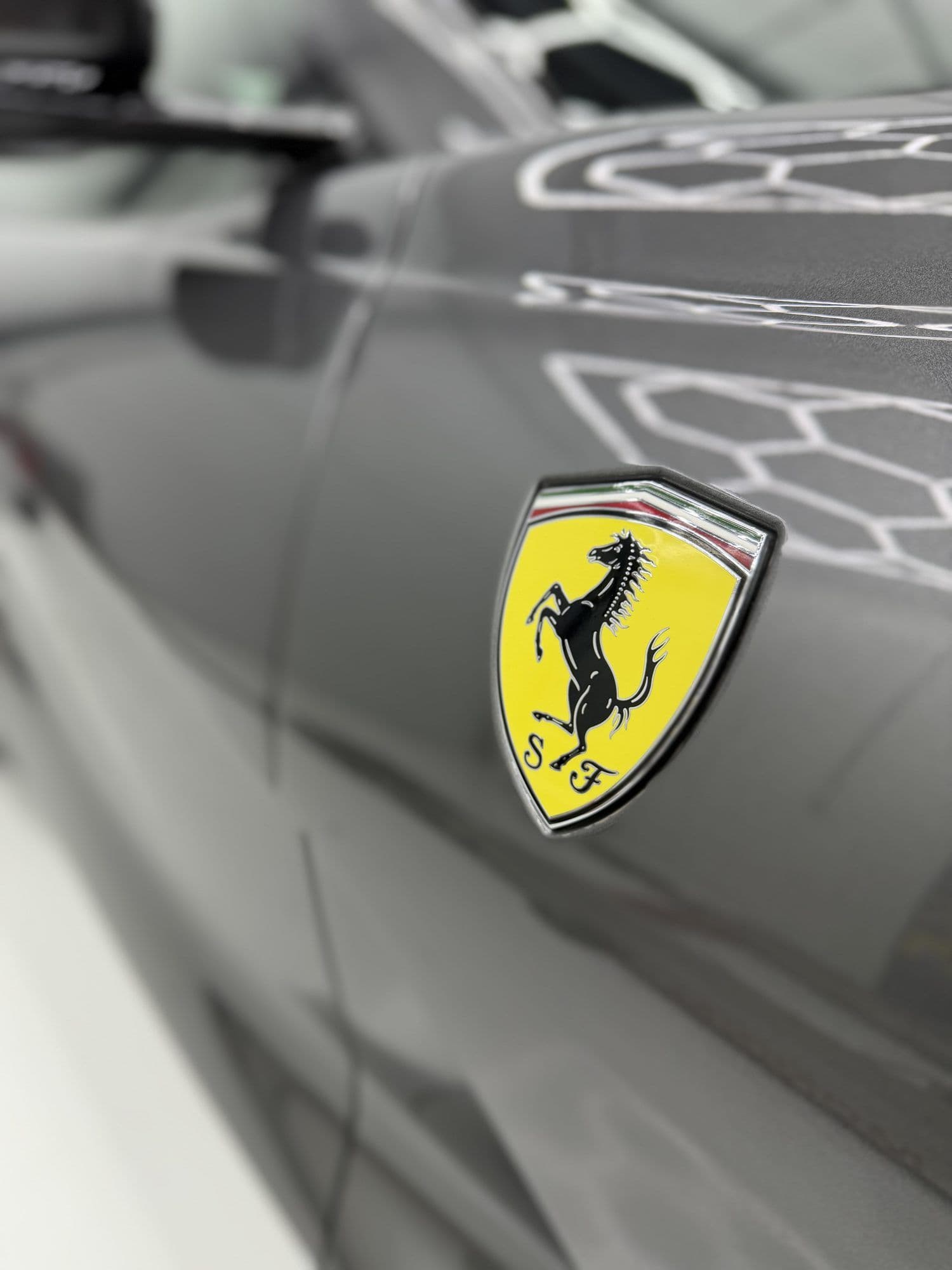 Ferrari-embleem op het grijze voorscherm van de 812 GTS, met de studioverlichting in de lak